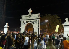 A fotografia mostra, em primeiro plano, uma multidão na frente da entrada do Cemitério São Bonifácio durante a noite. Ao fundo, estão árvores e túmulos.